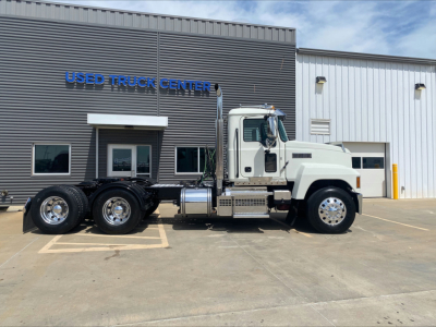 Mack PI64T conventional daycab truck side view with white cab and dual rear axles parked in front of a used truck center building.