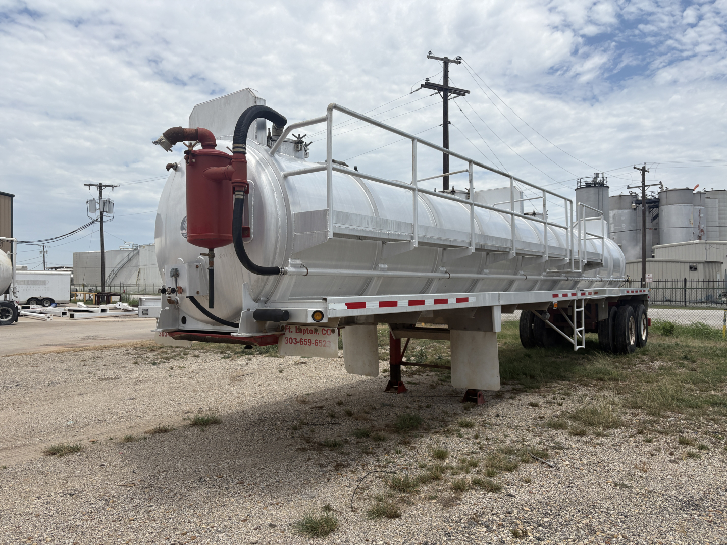 Tank trailer showing large cylindrical aluminum vacuum tank with rear red pump and walking catwalk on top, tandem axles in background.