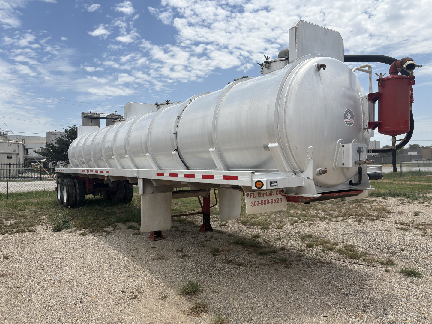 Horizontal cylindrical vacuum trailer with silver tank, red fire extinguisher on rear, landing gear and dual axle wheels visible.