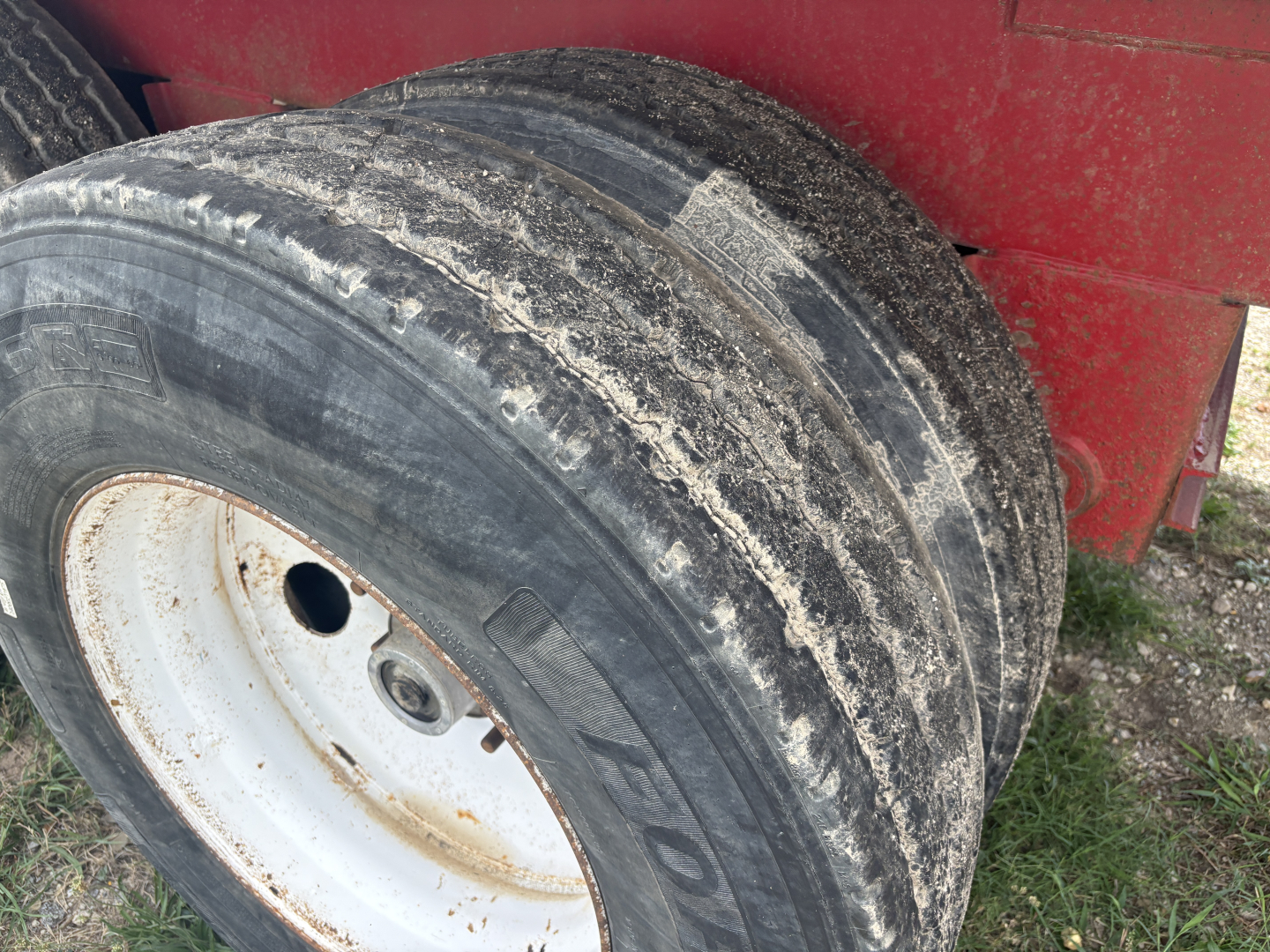 Trailer wheel showing worn dual tires and white wheel rim on red tank trailer.