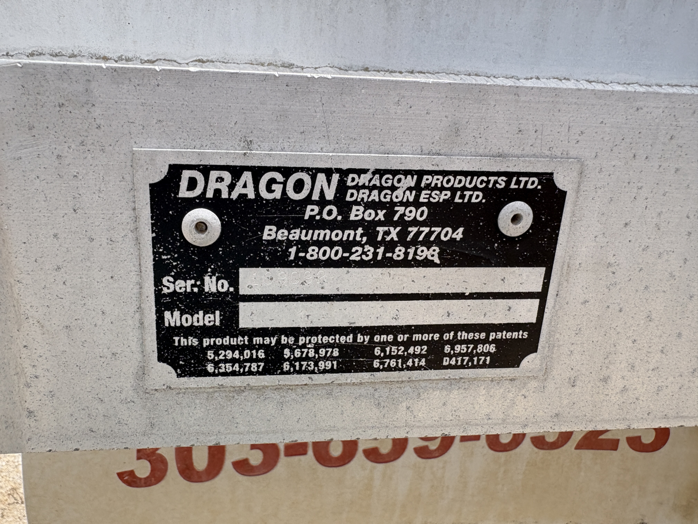 Metal plate with Dragon Products Ltd. branding and P.O. Box address; serial number and model fields blank; shows phone number 1-800-231-8196; background also shows partial red numbers.