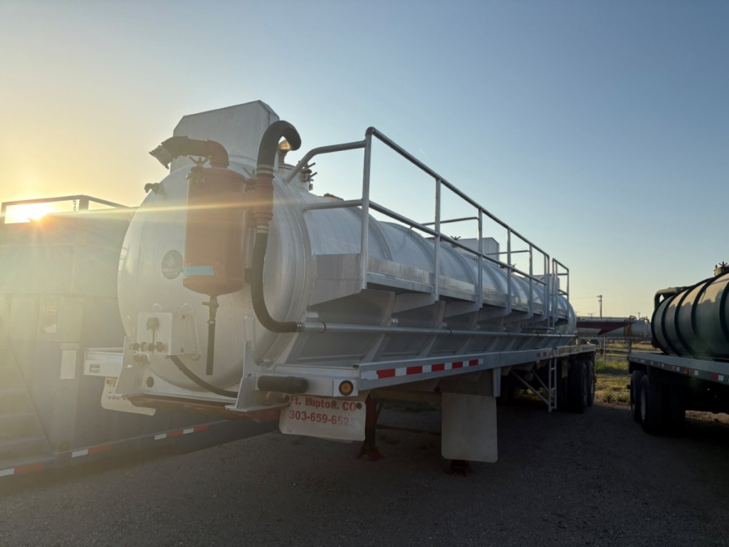 Trailer showing a Dragon 150BBL Vacuum tanker with railing on top, rear pump, and side ladder, labeled equipment visible in sunlight