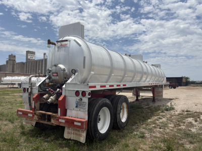 Rear/side view of a 2012 Dragon 150BBL Vacuum trailer with cylindrical stainless steel tank, dual rear axles, and mud flaps; VIN placard and stock number visible.