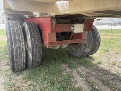 Trailer undercarriage showing dual rear axles with two tires on each side and red frame portion.