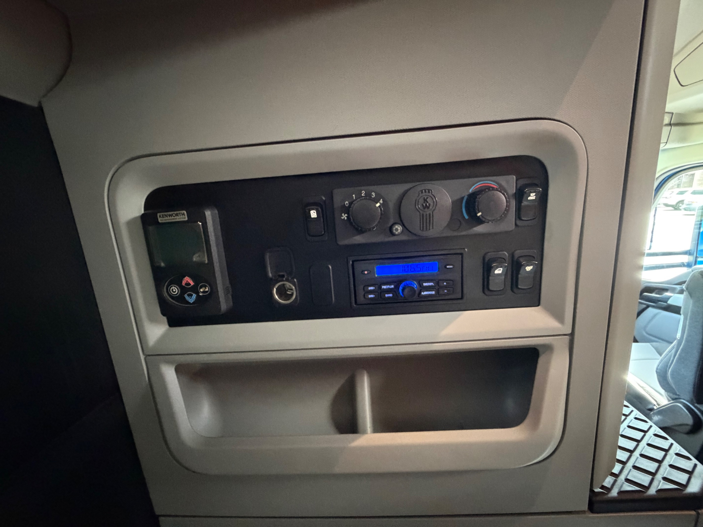 Kenworth T680 cab interior panel showing controls, radio, climate knobs, USB/aux ports, and a small storage compartment.