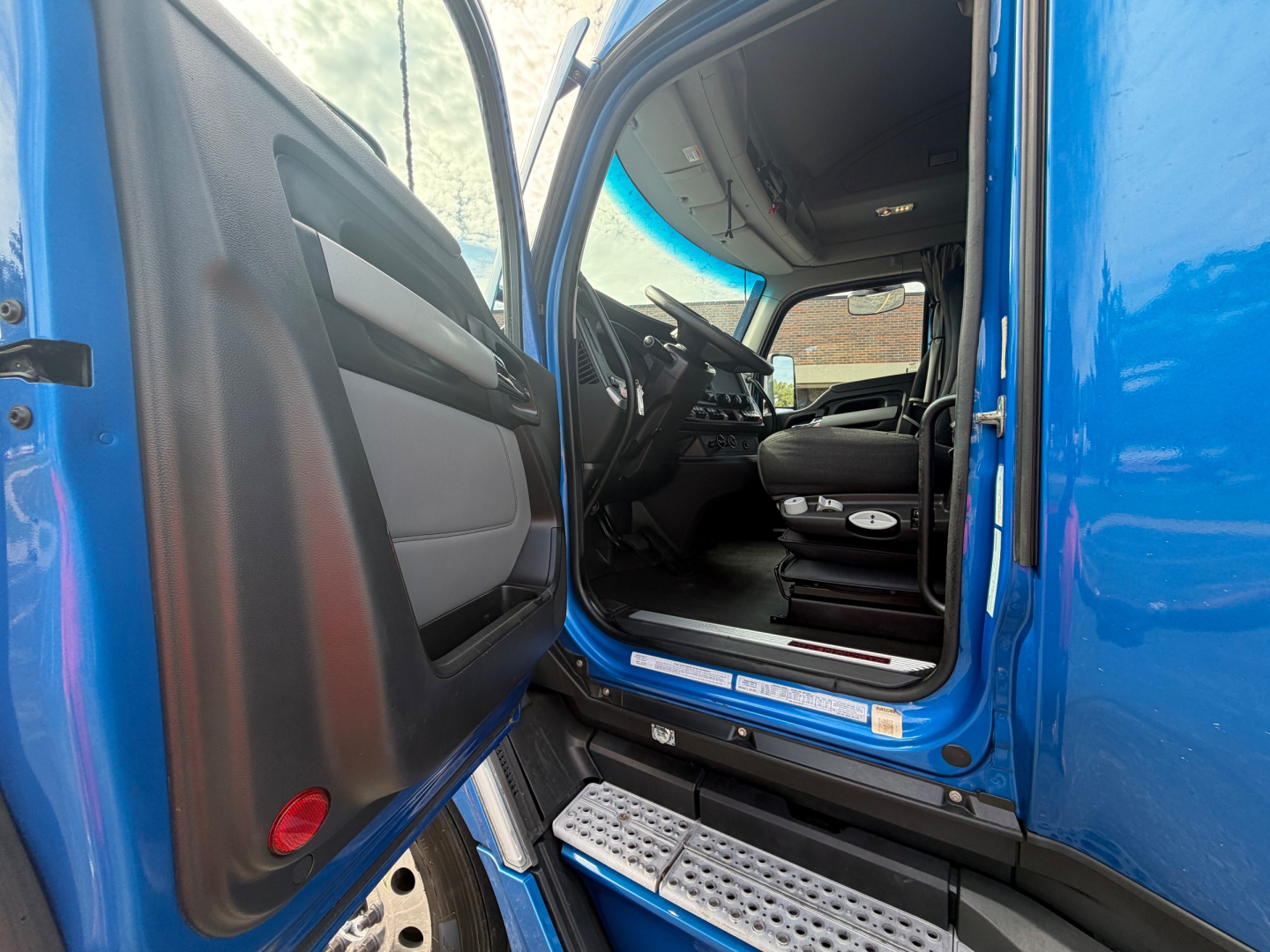 Kenworth T680 truck cab interior seen from open driver door showing seating and dashboard; blue exterior; steps and door area visible.
