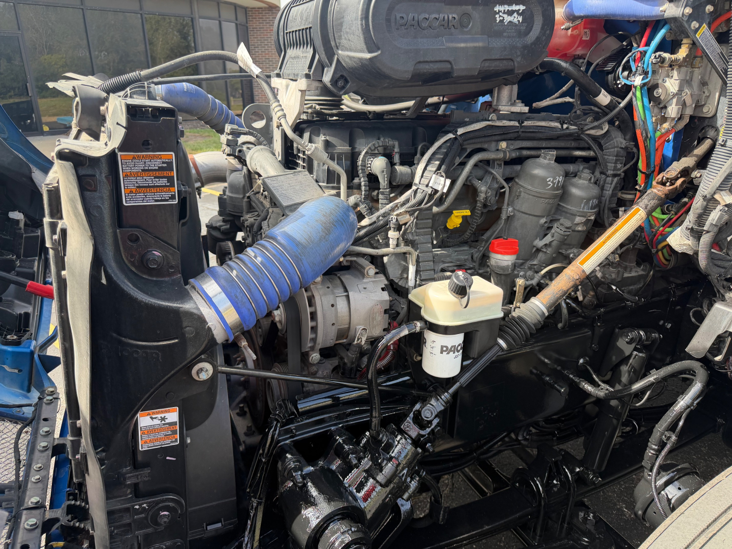 Kenworth T680 engine bay showing turbocharger, hoses, coolant reservoir, and various engine components with labeled stickers visible.