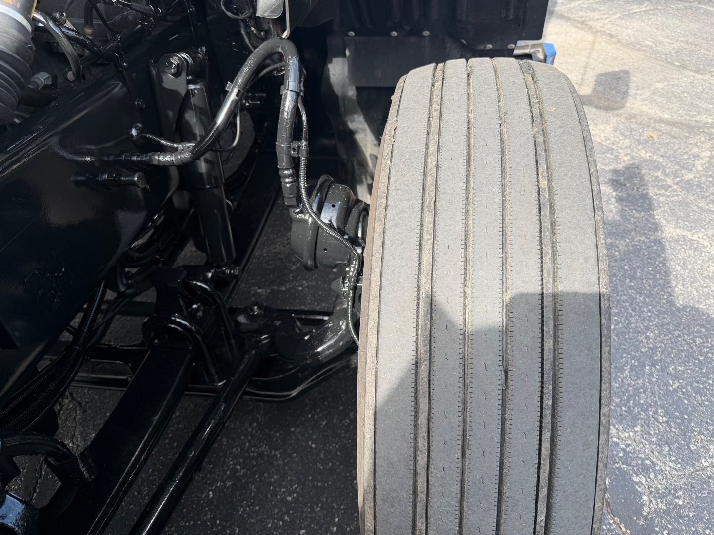 Kenworth T680 front left wheel area showing suspension components and chassis with wiring harnesses visible.