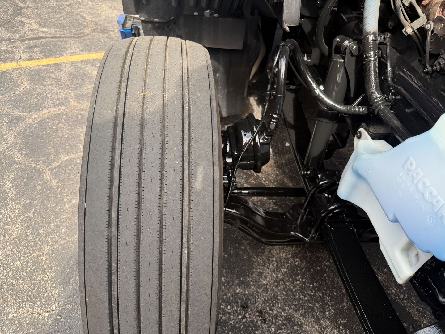 Kenworth T680 front left wheel and suspension components visible with coolant reservoir cap in view.