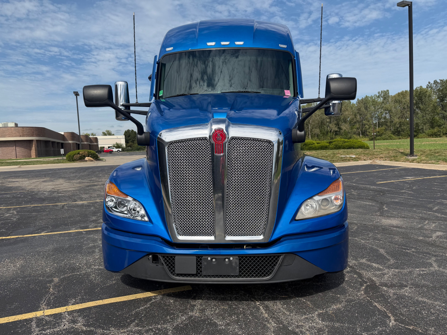 Front view of a blue 2023 Kenworth T680 truck in a parking lot showing the grille, headlights, and bumper.