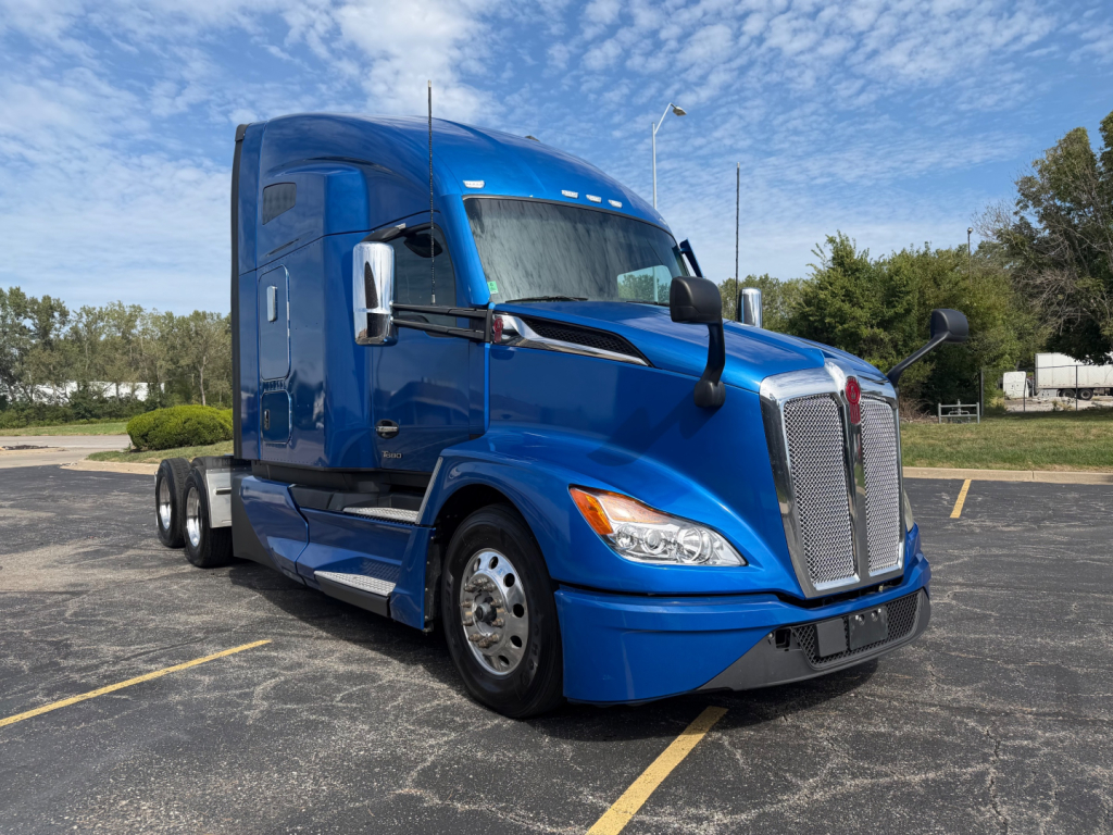 Kenworth T680 tractor in blue, front three-quarter view, showing tall sleeper cab, large grille, chrome mirrors, and dual rear axles.