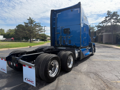 Kenworth T680 conventional sleeper tractor in blue, rear drive axles visible, showing truck chassis and cab from a rear-side angle.