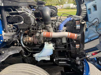 Kenworth T680 engine bay showing coolant reservoir, air intake, turbo, intercooler hose, and blue coolant expansion tank.