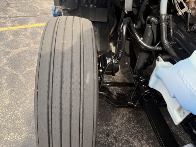 Kenworth T680 front left wheel and suspension components visible with coolant reservoir cap in view.