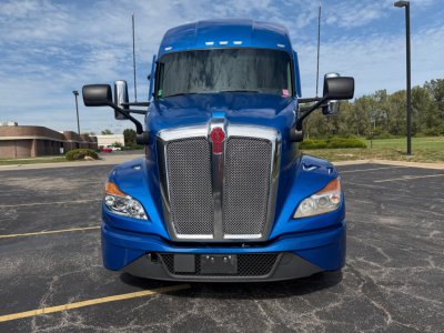 Front view of a blue 2023 Kenworth T680 truck in a parking lot showing the grille, headlights, and bumper.