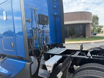 Kenworth T680 cab exterior side view showing steps, air lines, electrical harnesses, and fuel/utility compartments in blue paint.
