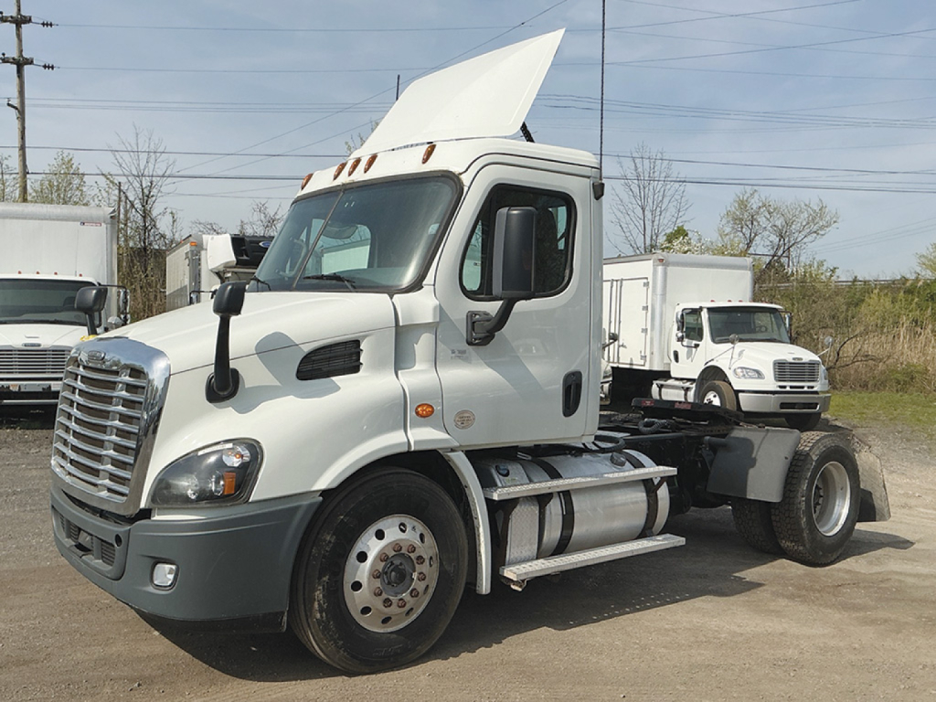 Truck cab and chassis of a Freightliner Cascadia 113 daycab with raised hood in a parking lot.