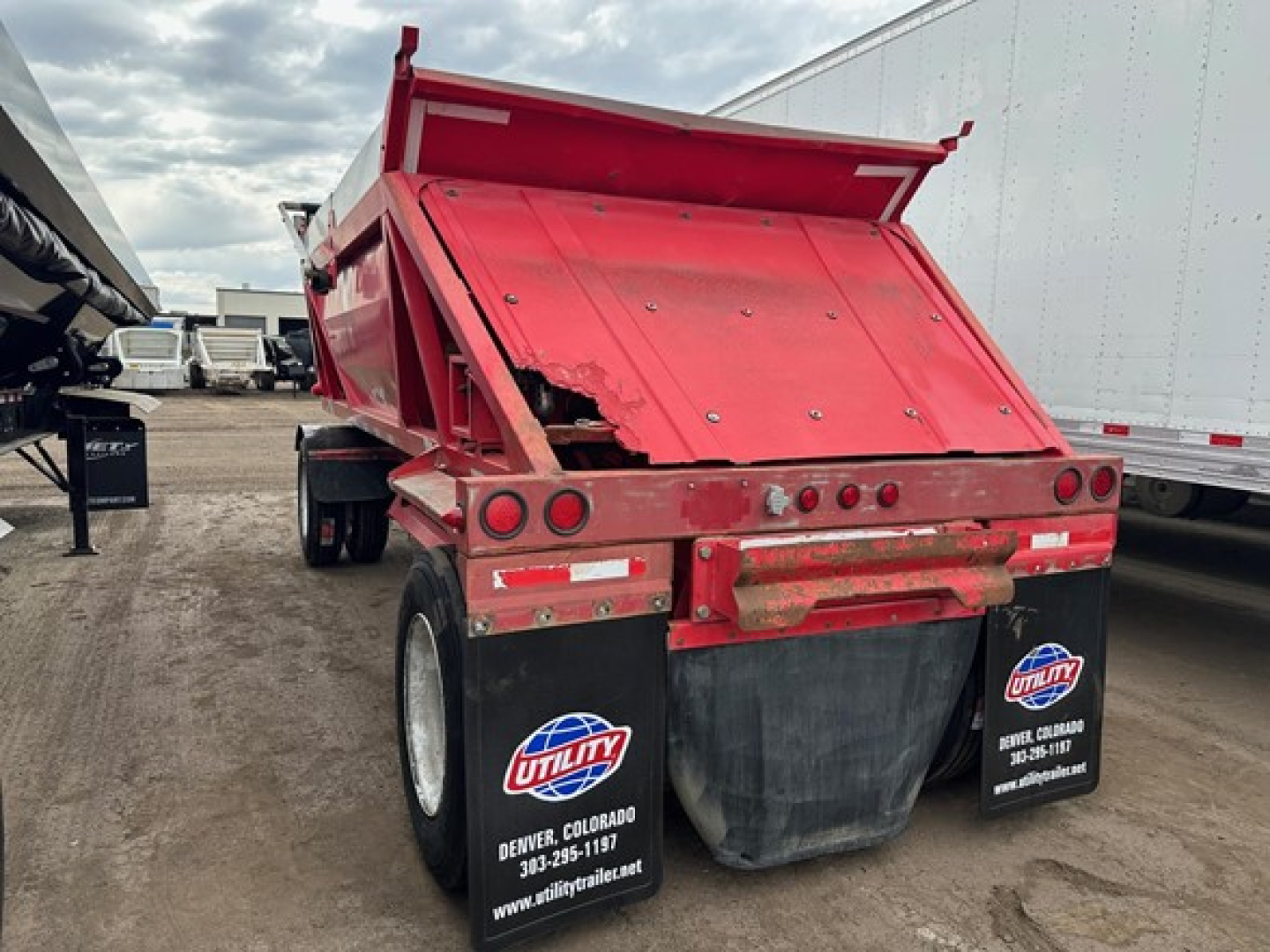 Dump trailer showing raised red steel bed and rear tailgate with two large black mud flaps and Utility trailer logos.