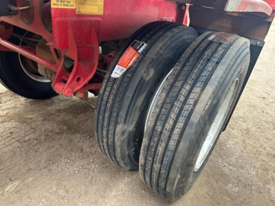 Dual trailer wheels and red chassis of a dump trailer showing tire tread and warning labels.