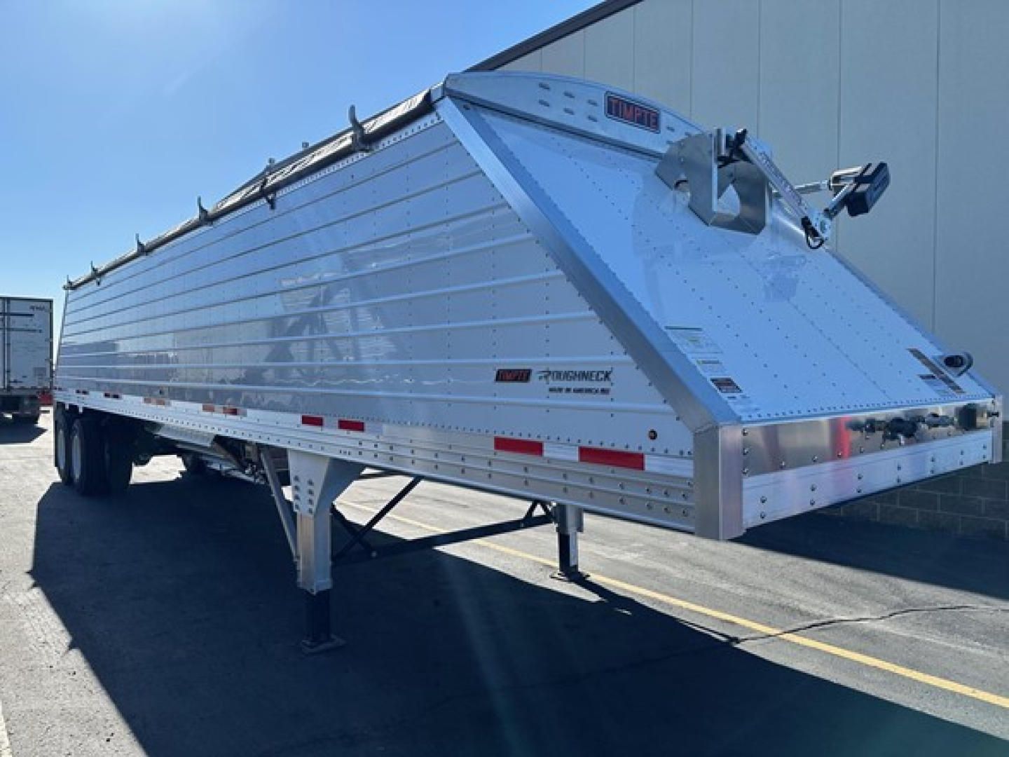 Timpte Roughneck hopper bottom sand trailer side view showing aluminum body, reflective strips, and front-mounted hitch assembly.