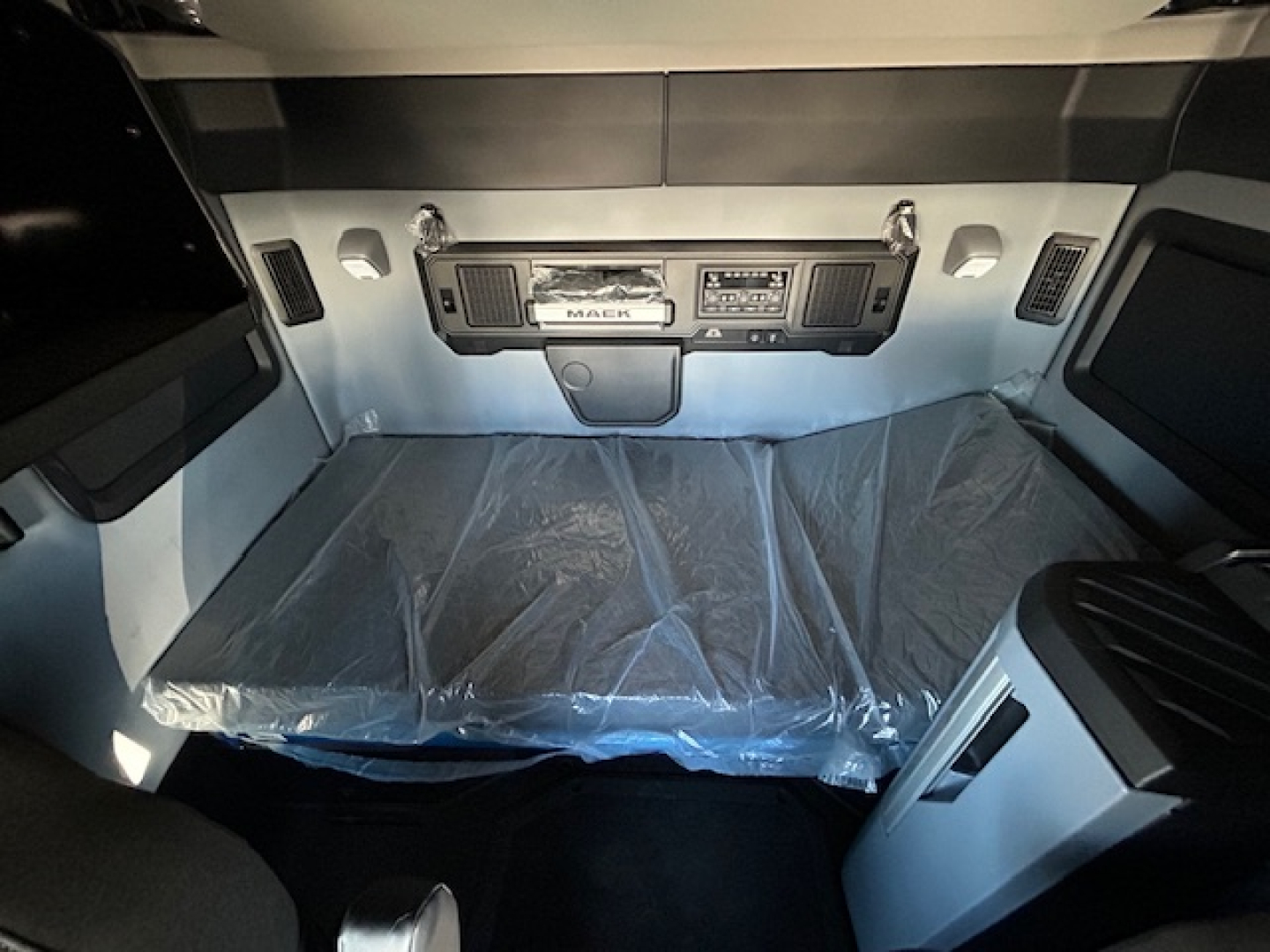 Mack PR64T64 truck cab interior view with sleeper area and dashboard controls visible, plastic covering on the bed.