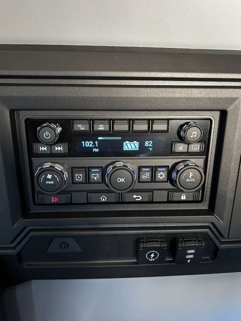 Dashboard radio and control cluster in a Mack PR64T64 truck showing station 102.1 FM, temperature 82, multiple buttons, and circular knobs.