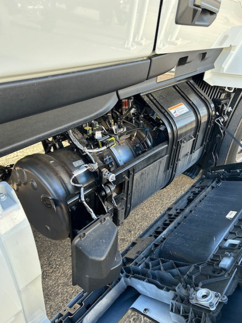Engine area of a new Mack PR64T64 cab crop showing fuel/air tanks and engine bay components under a truck hood.