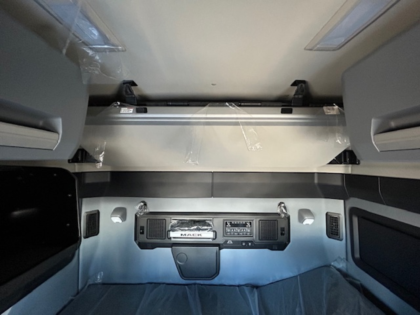 Truck cab interior showing dashboard and overhead storage area with Mack branding in a new conventional sleeper truck.