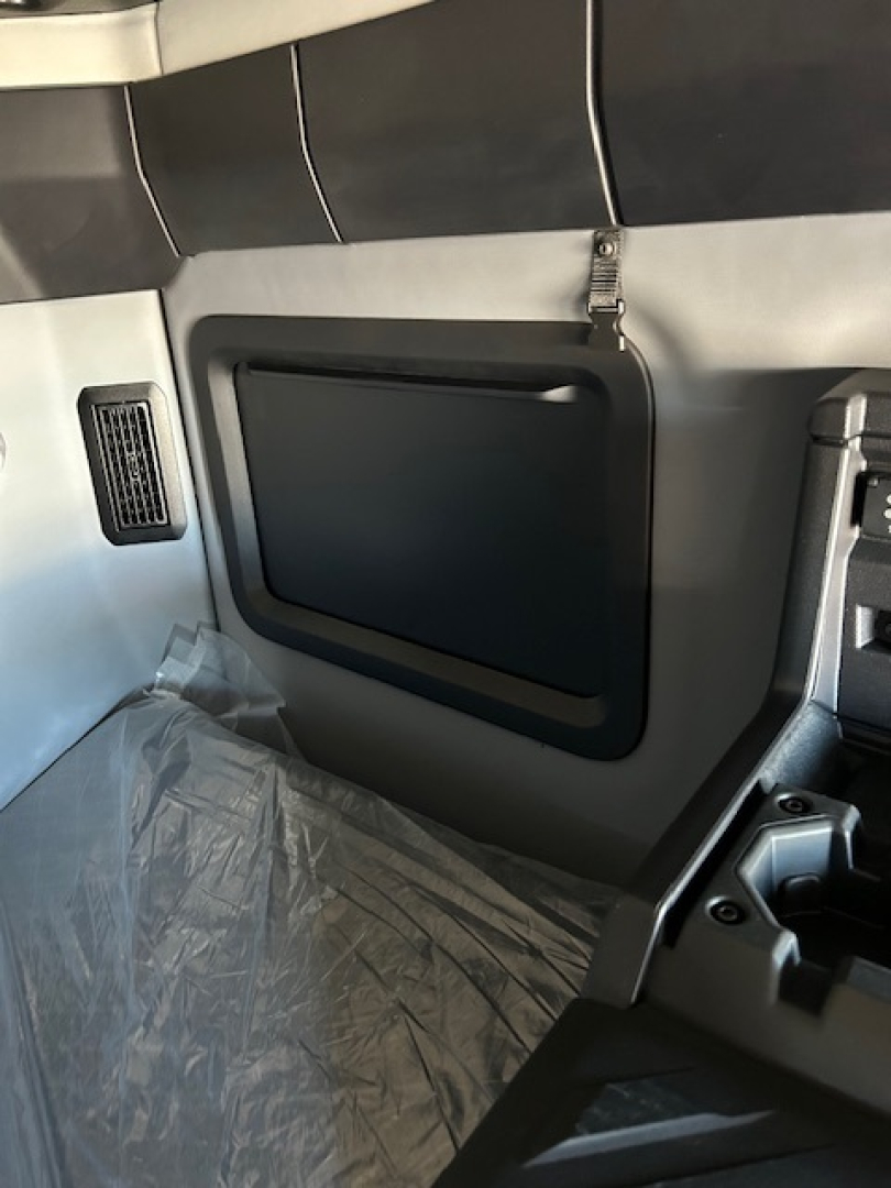 Truck interior side panel with storage pocket and window shade, cab wall, plastic floor cover, and seat area visible.