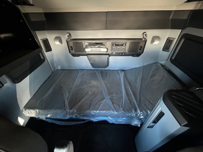 Mack PR64T64 truck cab interior view with sleeper area and dashboard controls visible, plastic covering on the bed.
