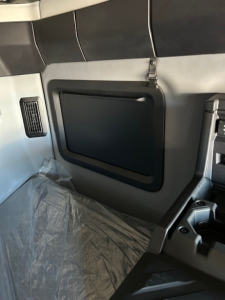 Truck interior side panel with storage pocket and window shade, cab wall, plastic floor cover, and seat area visible.