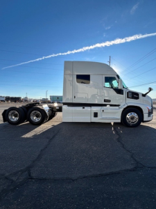Semi truck tractor in side view showing a gray Mack PR64T64 cab with sleeper, wheels, and attached trailer chassis.