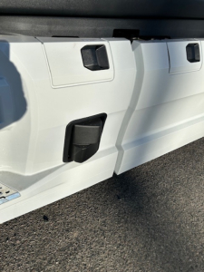 Tractor-trailer side panel showing utility access doors and black latches on a white Mack PR64T64 cab/chassis.