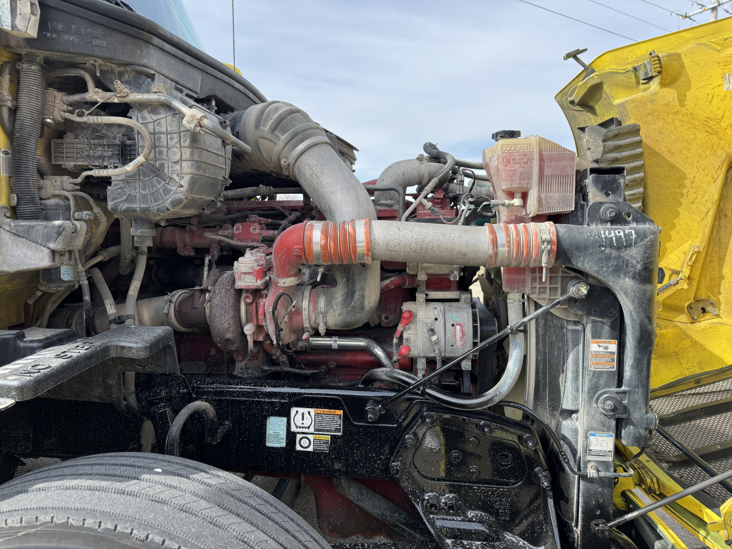 Peterbilt 579 engine bay view with turbocharger, intake piping, and radiator fan; multiple hoses and electrical harnesses visible under hood.