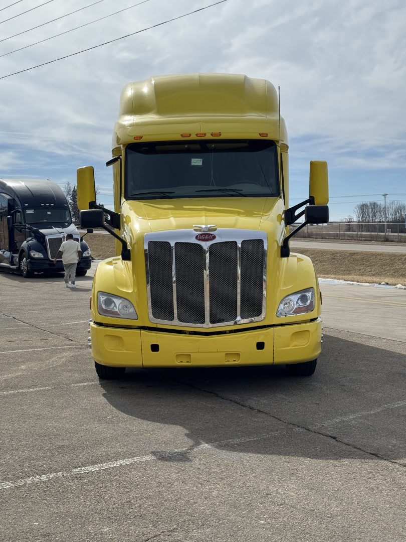 Peterbilt 579 conventional sleeper truck in yellow, front view with grille, headlights, and large hood.