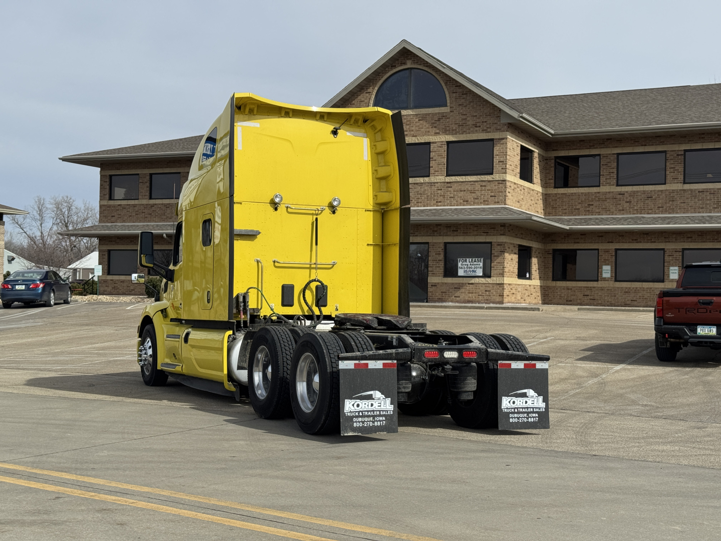 Peterbilt 579 tractor in bright yellow, rear view showing fifth wheel and triple rear axles, stock photo in lot