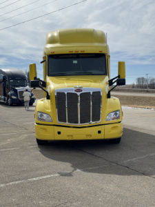 Peterbilt 579 conventional sleeper truck in yellow, front view with grille, headlights, and large hood.