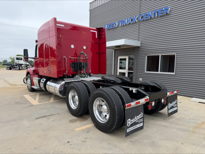 Peterbilt 579 tractor with red cab and dual rear axles, viewed from rear-left, parked outside a Used Truck Center.