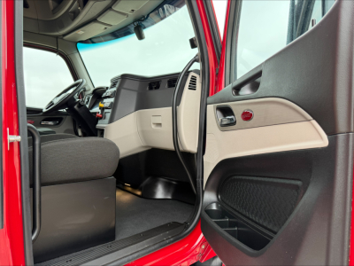 Peterbilt 579 truck cab interior view showing steering wheel, dashboard, beige door panel, and open driver’s seat area.
