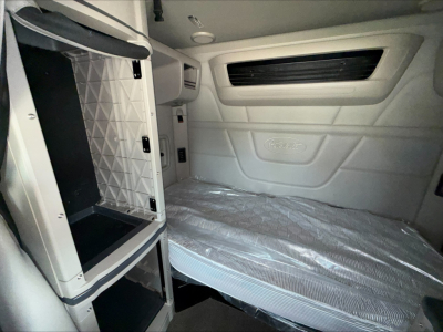 Peterbilt 579 sleeper cab interior showing side storage cabinet and bed with mattress in plastic wrap.