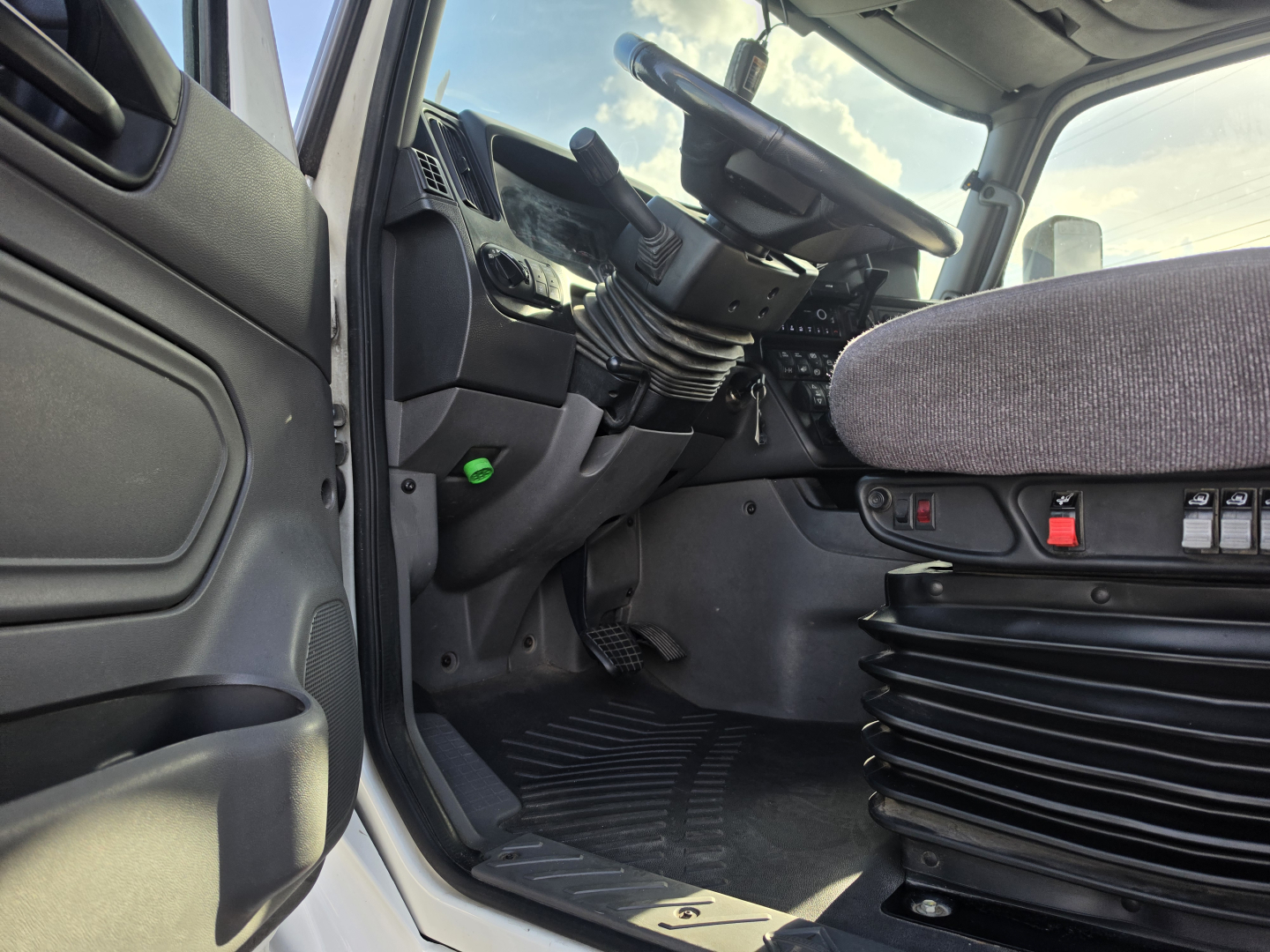 Interior of a truck cab showing driver seat, steering wheel, pedals, and center console in view.