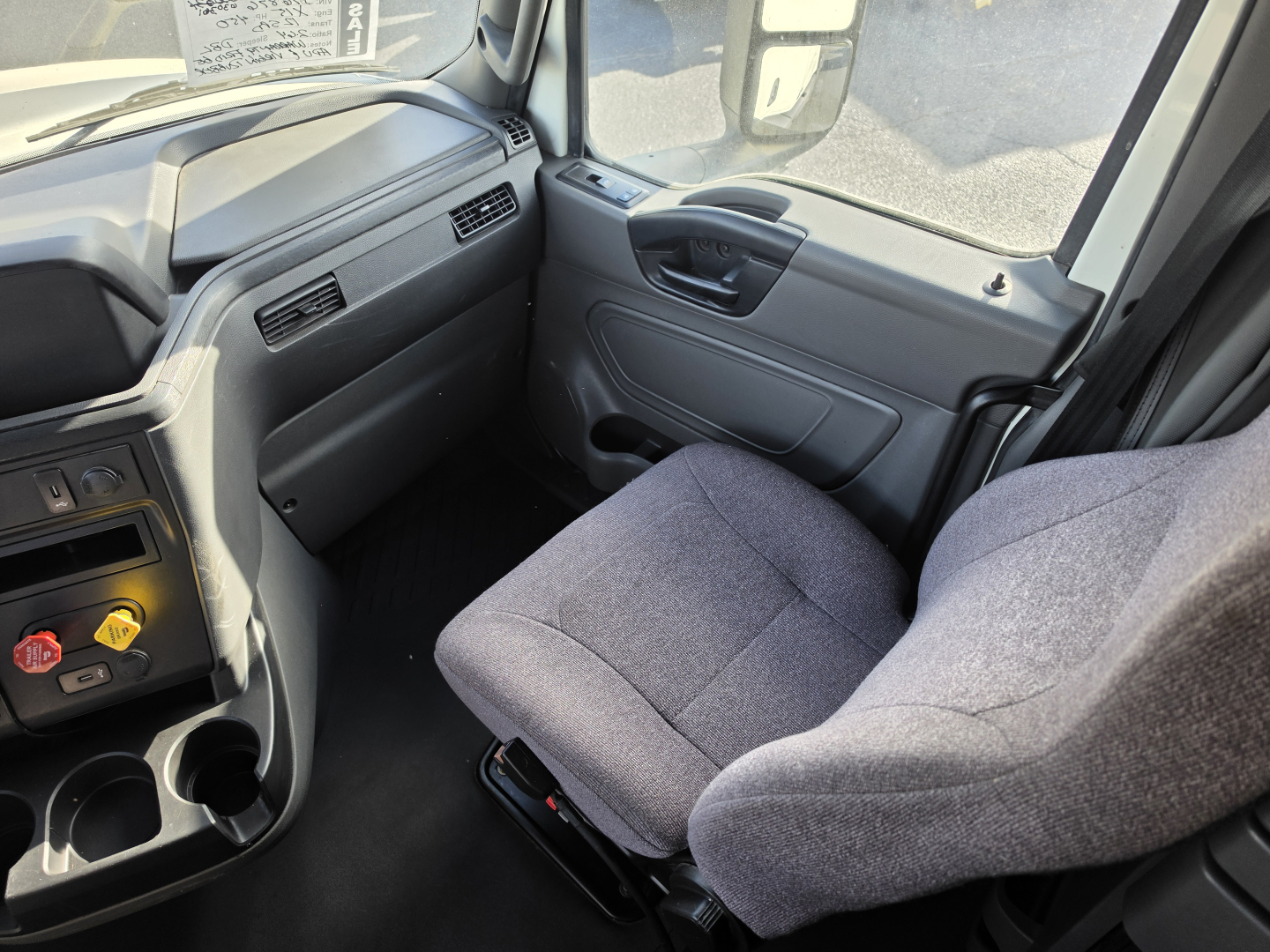Truck cabin interior with gray fabric seat, dashboard vents, and cupholders visible in a cab-view of a 2023 International LT625.