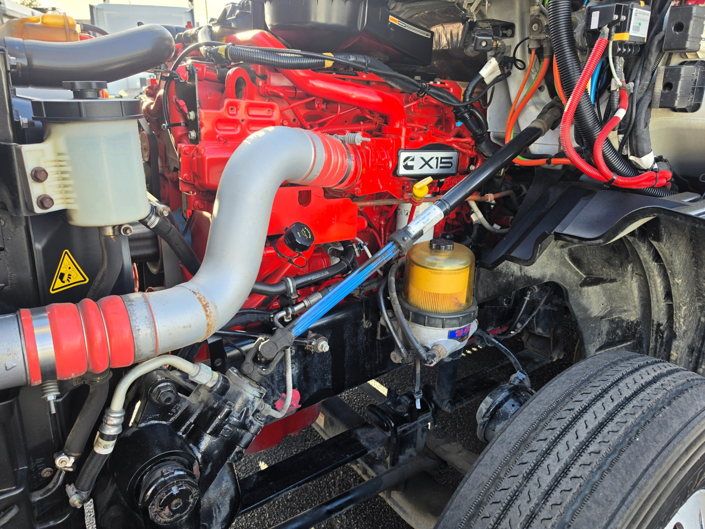 International LT625 engine bay showing bright red engine with grey intake pipe, yellow oil filter, and various hoses and wiring in a truck engine compartment.