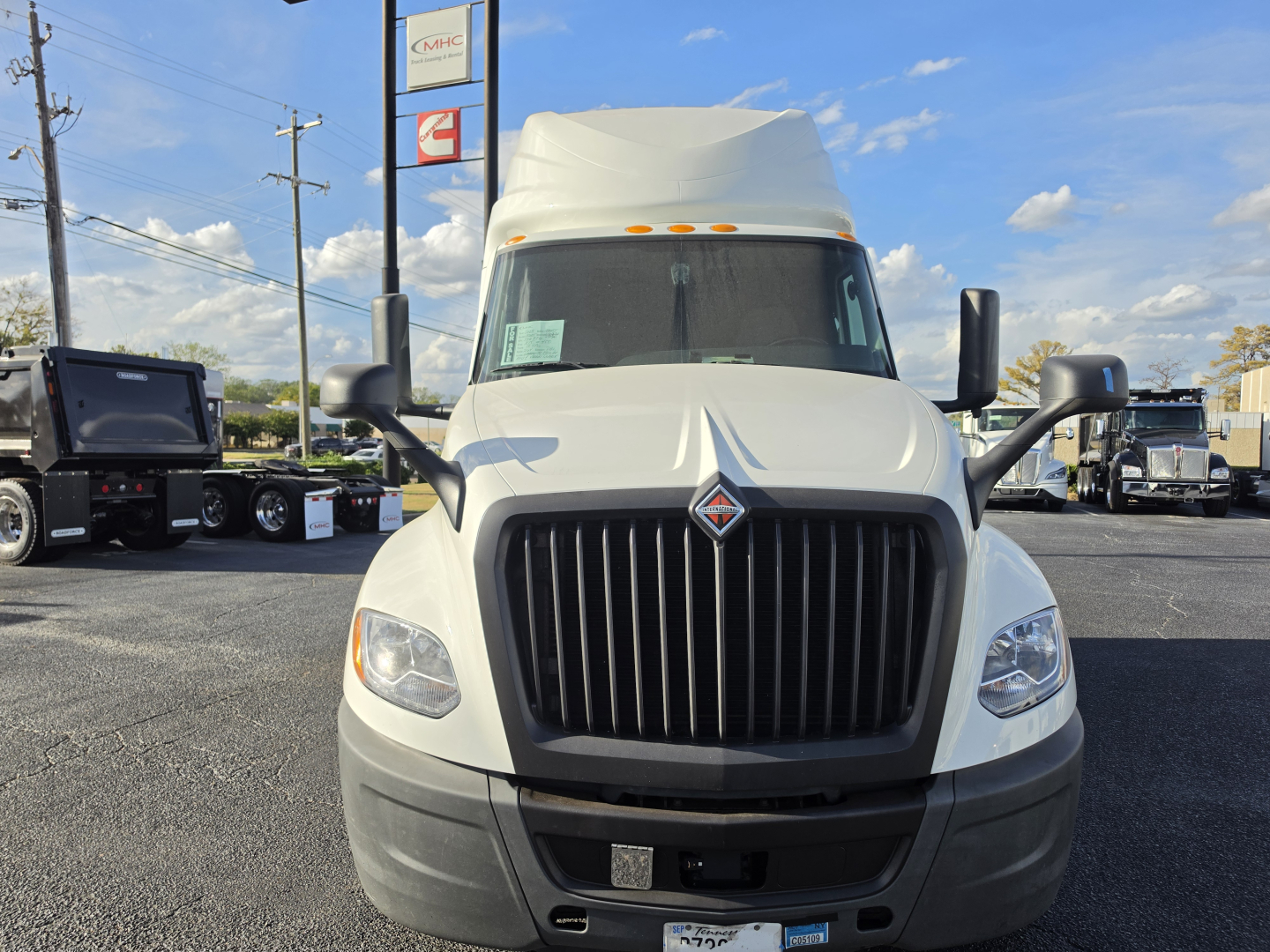 Front view of a white 2023 International LT625 sleeper cab truck with large vertical grille, black bumper, and side mirrors in a dealership lot.