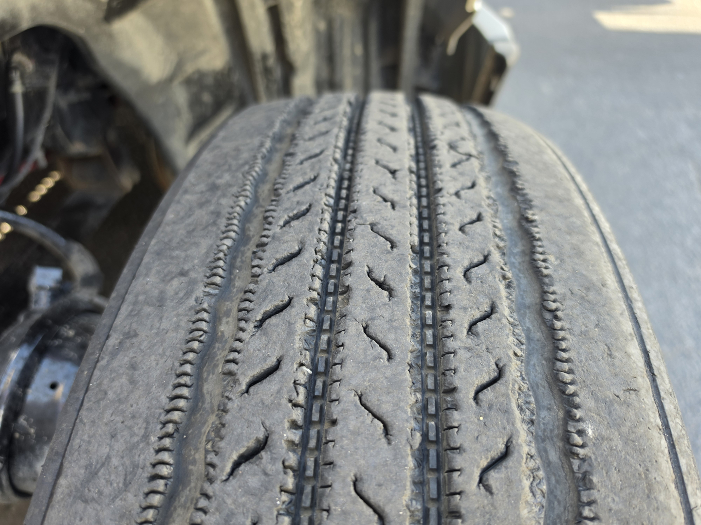 Truck tire in service showing tread wear and sidewall; part of International LT625 cab and suspension visible in background.
