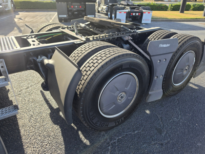 Truck chassis rear showing dual rear axles with heavy tires and wheel covers, fuel tanks, and Frameless mud flaps near the fifth wheel area.