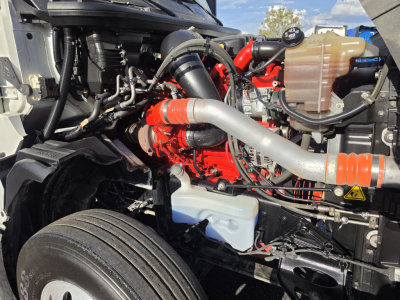 Truck engine bay with bright red engine block, large intake hose, coolant reservoir, and various hydraulic lines visible.