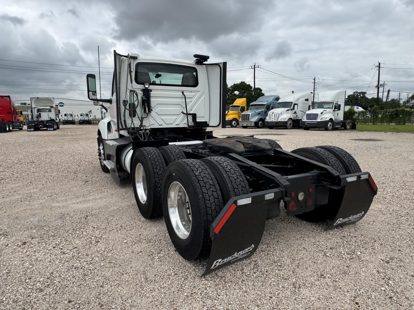 Truck cab rear view showing dual rear axles and fifth-wheel chassis with mud flaps reading Beneath-Bego? and road grime on the tires.