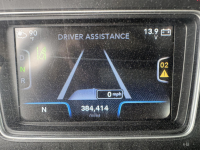 Dashboard display showing Driver Assistance with a vehicle centered on a road, 0 mph, N gear indicator, 384,414 miles, 90°F outside, 13.9V on the right, warning icon on the passenger side.