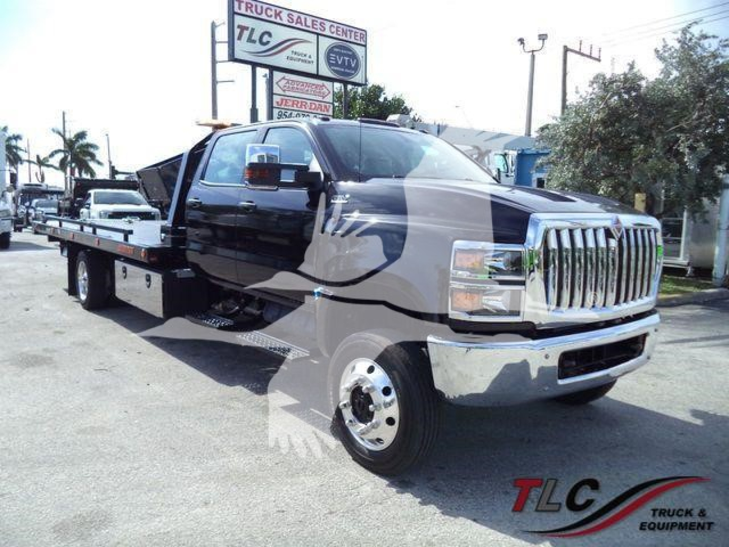 2023 International CV truck in a rollback configuration with dual rear wheels, chrome grille, and extended cab. Visible text includes TLC Truck Sales Center sign in background.